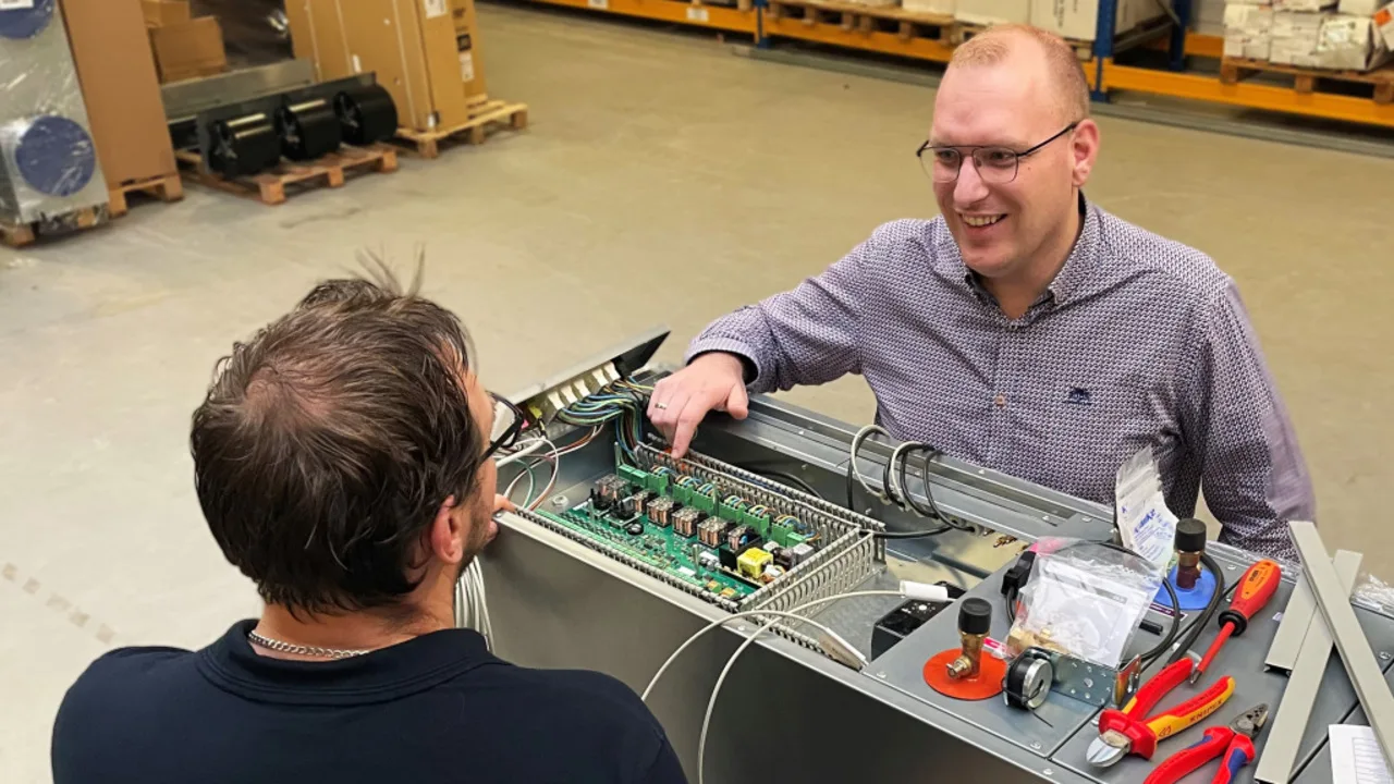 Harmen in gesprek met een collega bij een open regelkast in de fabriek